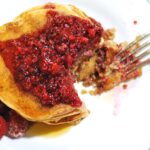 Stack of almond butter pancakes topped with raspberries with a bite taken out of them