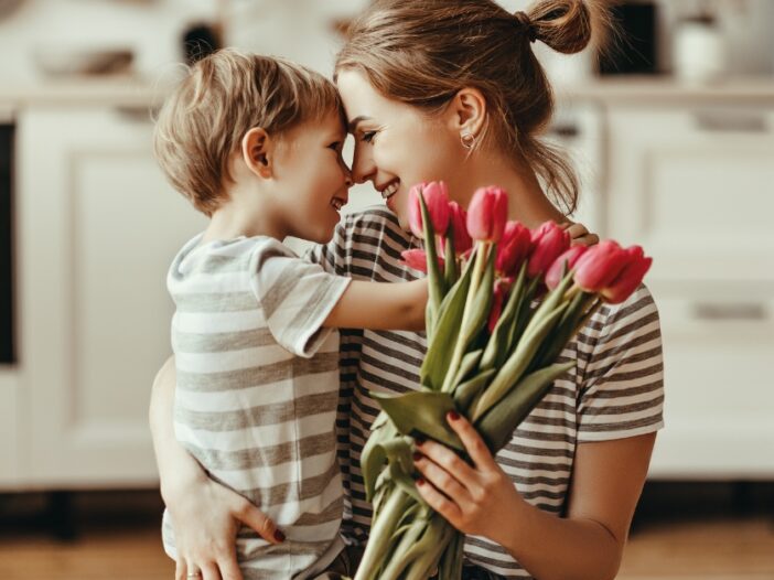 Woman holding a young boy closely and touching foreheads. She is also holding a bunch of tulips