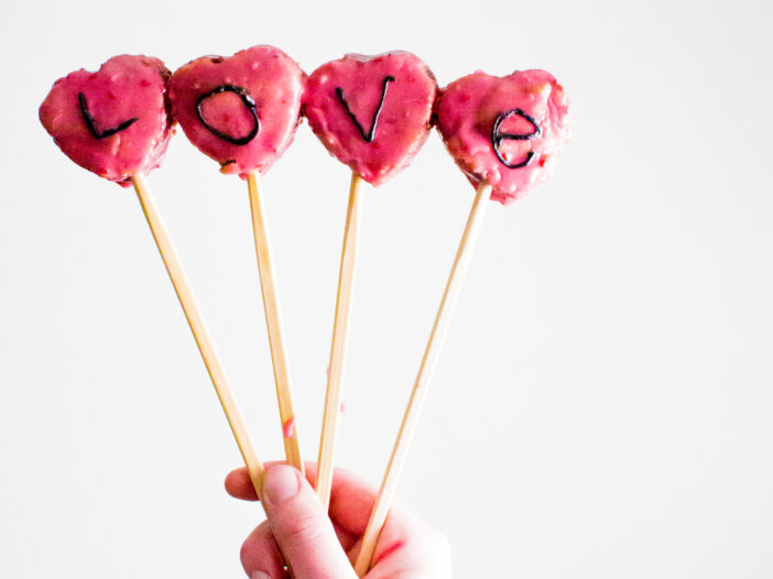 Four Raspberry Conversation Heart Pops on wooden skewers spelling out the word Love