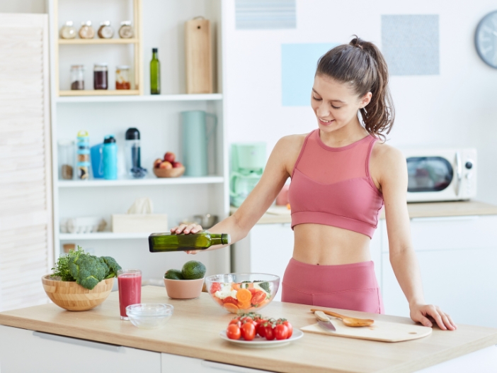 Woman standing in kitchen in exercise clothes pouring oil into a bowl