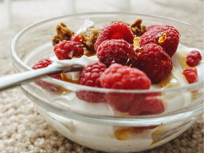 Clear bowl full with yogurt, topped with raspberries and drizzled with honey