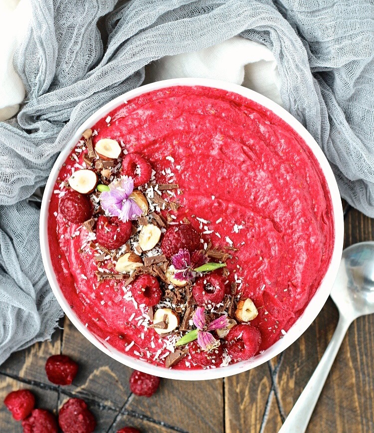 Raspberry Coconut Smoothie Bowl garnished with raspberries, flowers, chopped almonds, chocolate and coconut