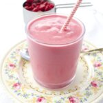 Raspberry Cheesecake Smoothie in short glass with a pink straw on a vintage plate decorated with flowers