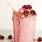 Overflowing glass of Raspberry Love Your Heart Frappe with a stripped pink and white straw
