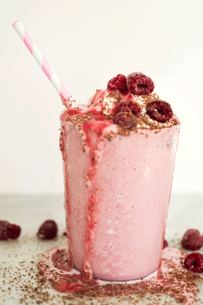 Overflowing glass of Raspberry Love Your Heart Frappe with a stripped pink and white straw