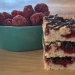 Three raspberry really bars stacked with bowl of frozen raspberries
