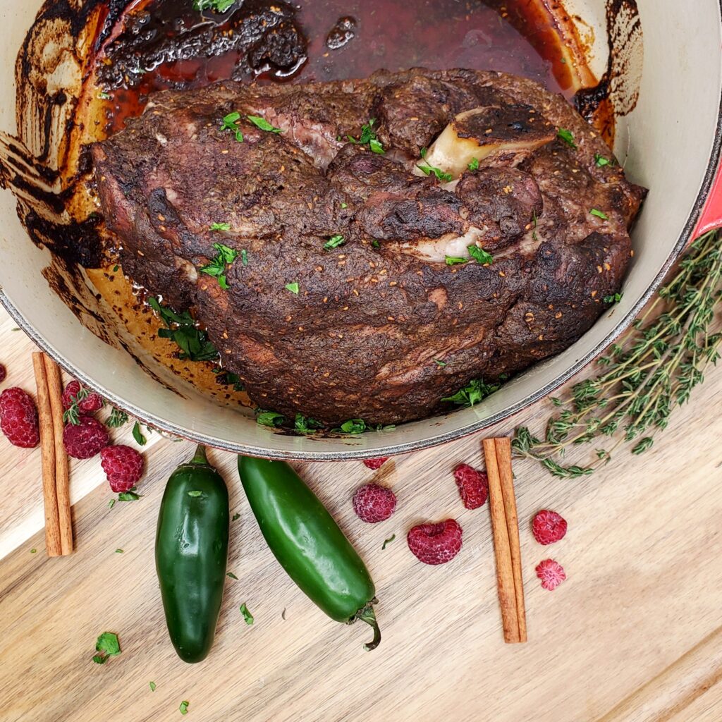 Raspberry Jerk Pork in dutch oven pot with cinnamon, jalapeno peppers and thyme on a wood table