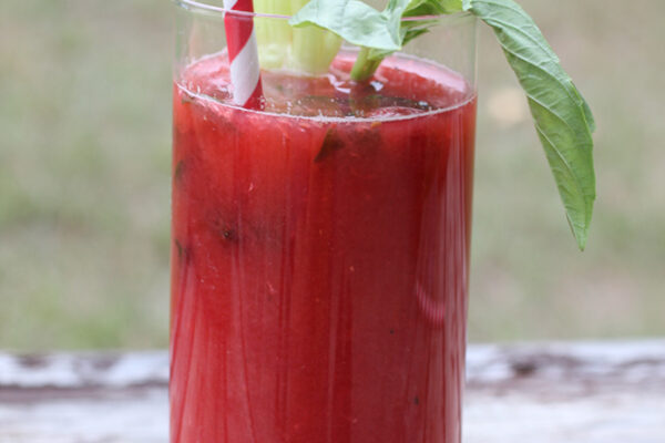 Virgin Razzy Mary in tall clear glass with red and white striped straw garnished with celery and basil