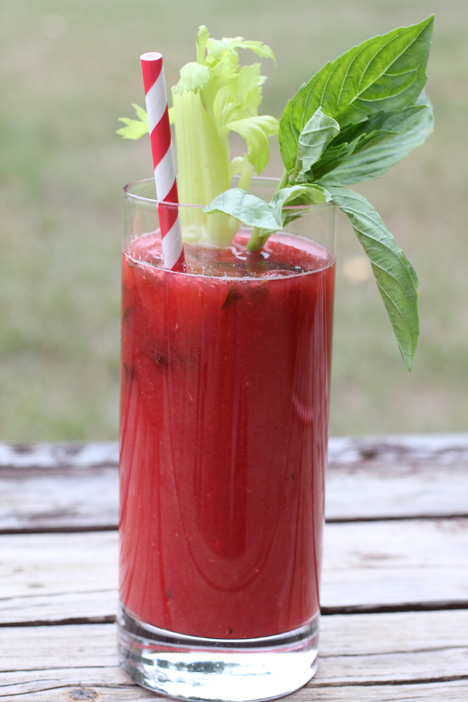 Virgin Razzy Mary in tall clear glass with red and white striped straw garnished with celery and basil