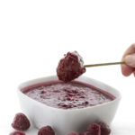Hand dipping Slow Cooker Meatballs into Raspberry Chipotle Dipping Sauce