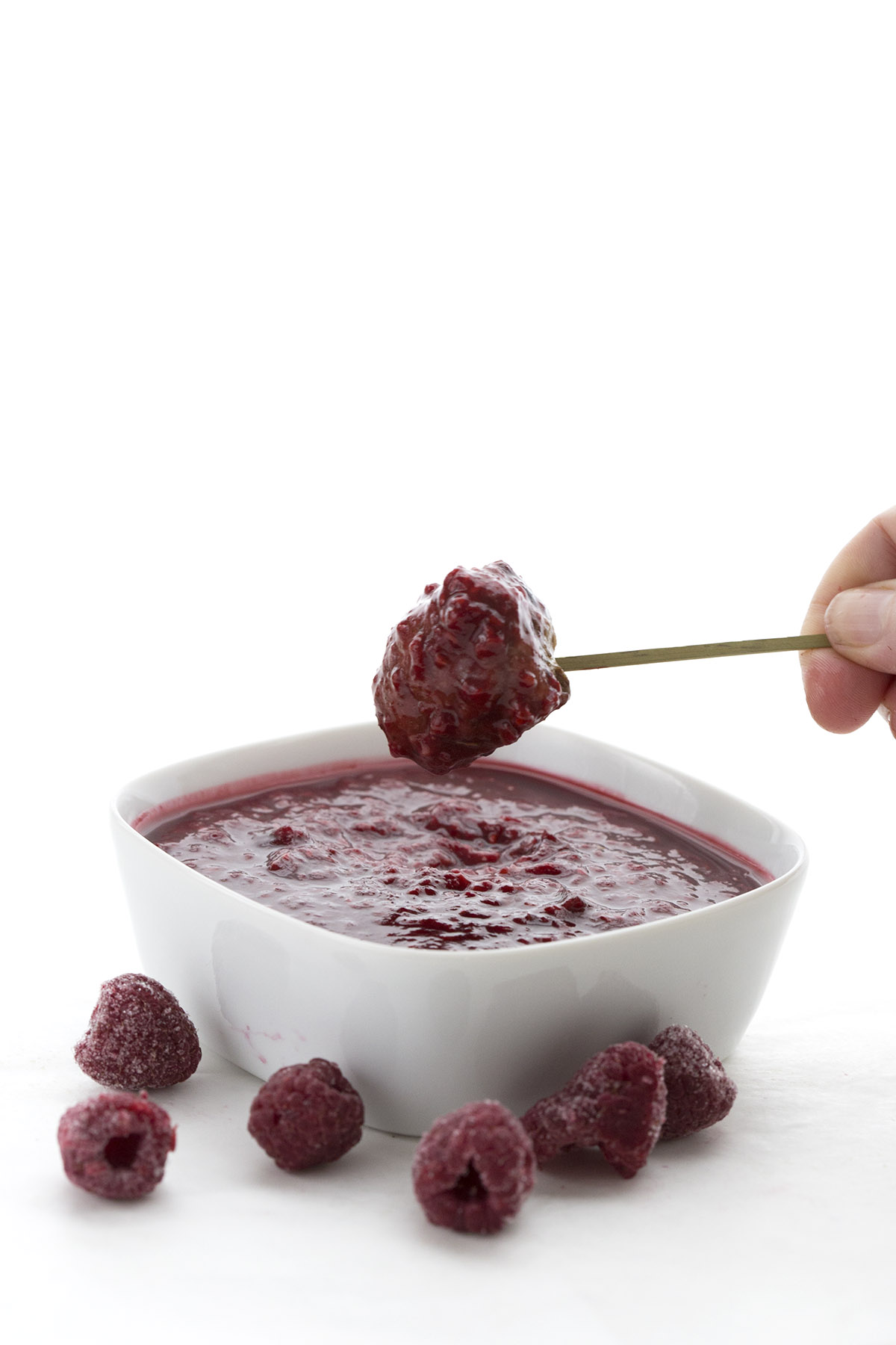 Hand dipping Slow Cooker Meatballs into Raspberry Chipotle Dipping Sauce
