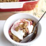Raspberry Apple Crisp with Brandy Sauce and Gingersnap Topping in white bowl topped with whipped cream
