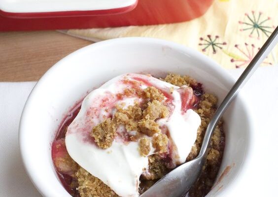 Raspberry Apple Crisp with Brandy Sauce and Gingersnap Topping in white bowl topped with whipped cream
