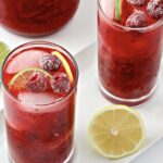 Two glasses of Razz Crush Red Party Punch garnished with raspberries, lime and lemon slices