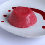 Raspberry Coconut Panna Cotta on white plate with drizzle of raspberry sauce
